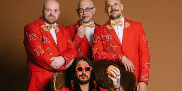 The 4 members of Elvana in red suits, with one in a chair with a burger in his hand.