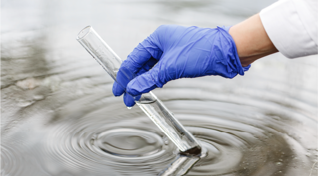 Mano recogiendo muestra de agua en tubo de ensayo