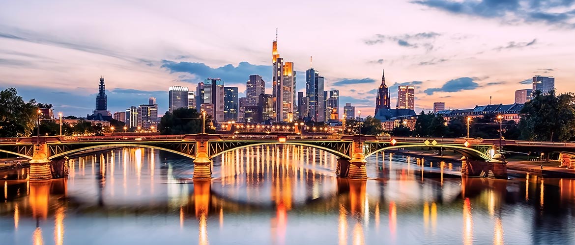 Abendlicher Blick auf die Skyline von Frankfurt am Main mit der beleuchteten Eisenbahnbrücke über dem Main – Symbolbild für juristische Präsenzveranstaltungen und Fortbildungen im Deutschen Anwaltsinstitut in Frankfurt