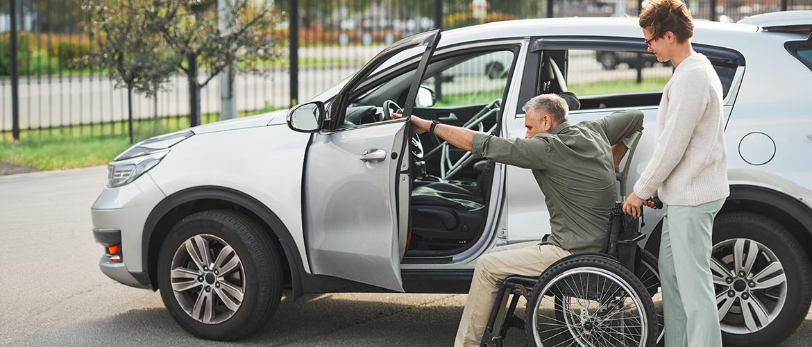 Unterstützung beim Einsteigen ins Auto, Person im Rollstuhl mit Begleitperson, Alltagshilfe, Fürsorge, Betreuung, Mobilität, familienrechtlicher Kontext. Fotorealistische Abbildung verwenden.