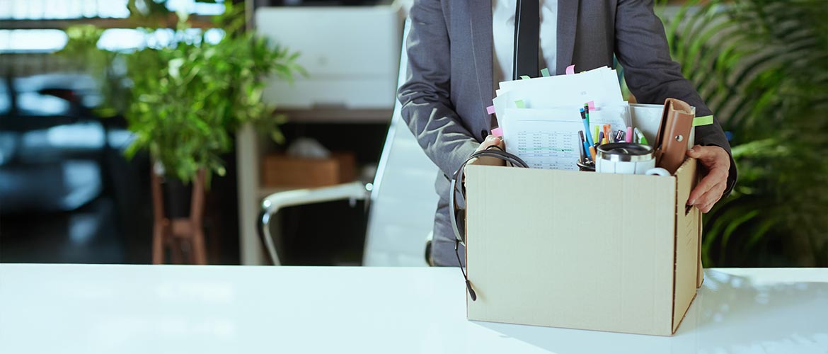 Person packt Schreibtischutensilien in einen Karton – Büro, Kündigung, Jobwechsel, Arbeitsplatzwechsel, Büroauszug, Karriere, HR.