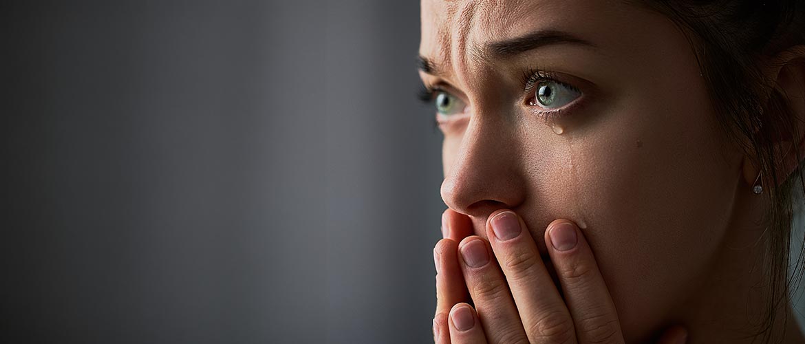 Fotorealistische Nahaufnahme einer Person mit Hand vor dem Mund, sichtbare Träne am Auge, weiches Licht, grauer Hintergrund, ausdrucksstarkes Porträt, SEO Bildbeschreibung. Fotorealistische Abbildung verwenden.