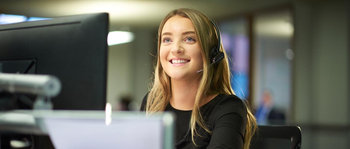 Lächelnde Frau mit Headset am Arbeitsplatz – Symbolbild für digitalen Service, Teilnehmerbetreuung und technischen Support rund um die Fortbildung im Deutschen Anwaltsinstitut