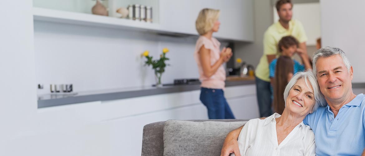 Senioren-Paar sitzt auf einem Sofa, im Hintergrund steht eine Frau in der Küche – Symbolbild für Trennung, familienrechtliche Fragestellungen und deren Behandlung in der Fortbildung im Deutschen Anwaltsinstitut