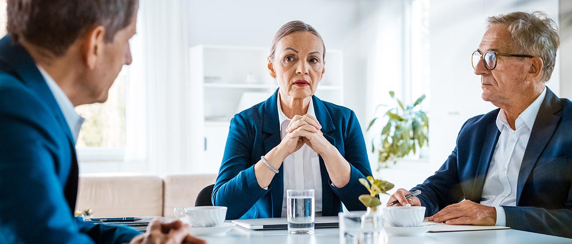 Besprechungsszene im modernen Büro, geschäftliches Meeting, professionelle Atmosphäre, Wasser- und Kaffeegläser am Tisch; fotorealistische Abbildung der teilnehmenden Personen.
