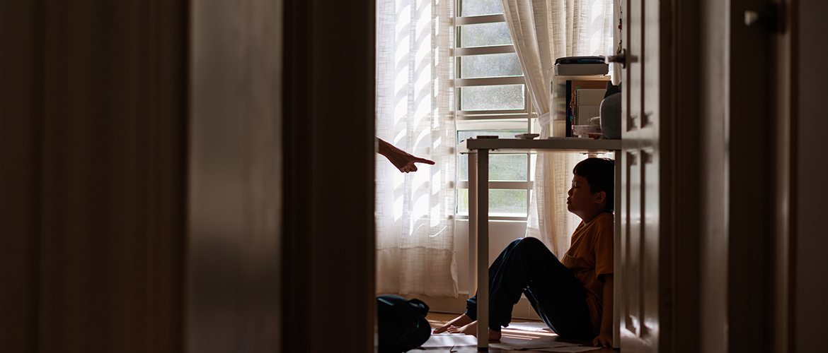 Fotorealistische Abbildung verwenden: Innenraum mit Kind unter einem Tisch, erwachsene Person zeigt mit Finger. Bedrohliche Situation, Familie, Kinderschutz, Gewaltprävention, soziale Themen.