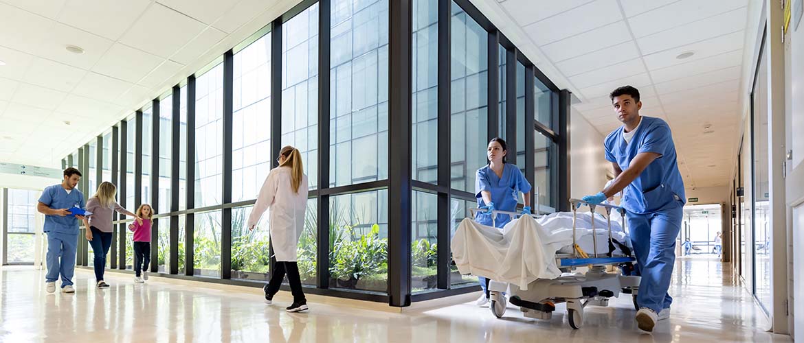 Bild eines Krankenhaus, innen, Ein Bett wird über den Flure geschoben, Patienten kommen einer Ärztin entgegen – Symbolbild für Medizinrecht, Klinikorganisation und rechtliche Fragestellungen im Gesundheitswesen in der Fortbildung im Deutschen Anwaltsinstitut