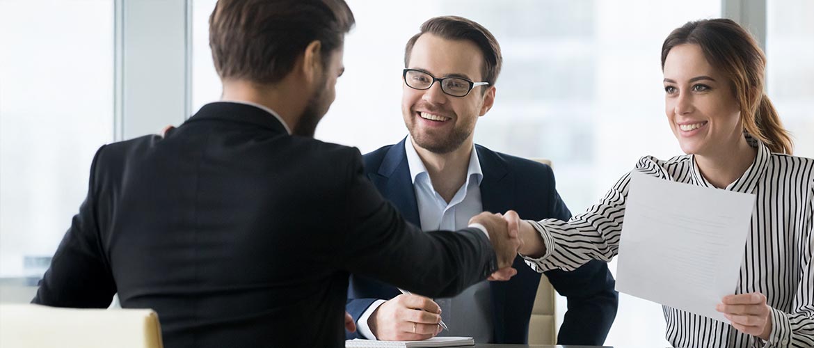 Lächelnder Mann in Businesskleidung vermittelt ein Gespräch zwischen zwei Händeschüttelnden – Symbolbild für Vertragsverhandlungen, rechtliche Beratung und juristische Einigung
