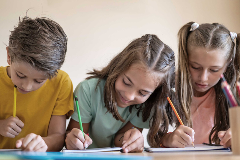Drei Kinder sitzen an einem Tisch und schreiben auf Papier