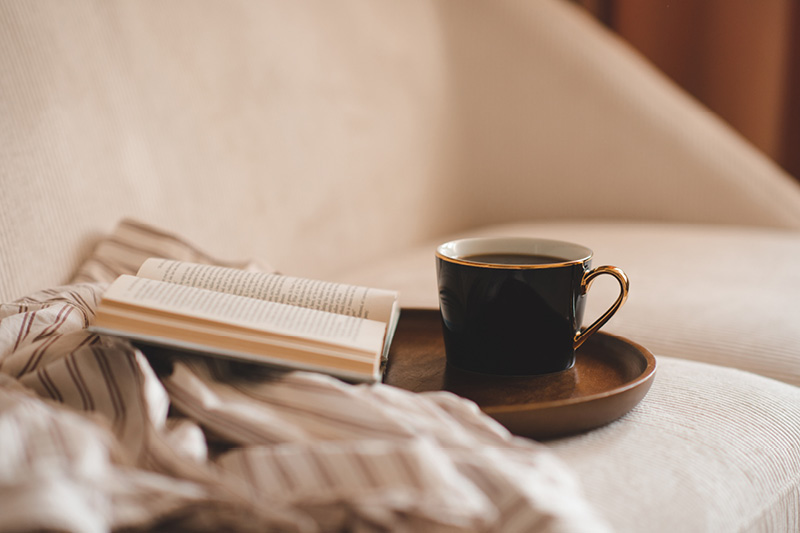 Eine Tasse Kaffee steht neben einem Buch auf einem Sofa