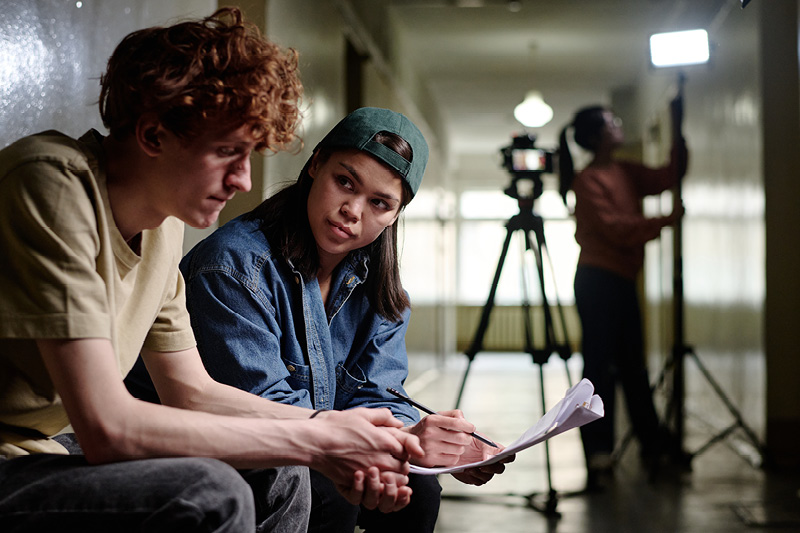 Eine Schülerin und ein Schüler sitzen vor einem Klassenzimmer