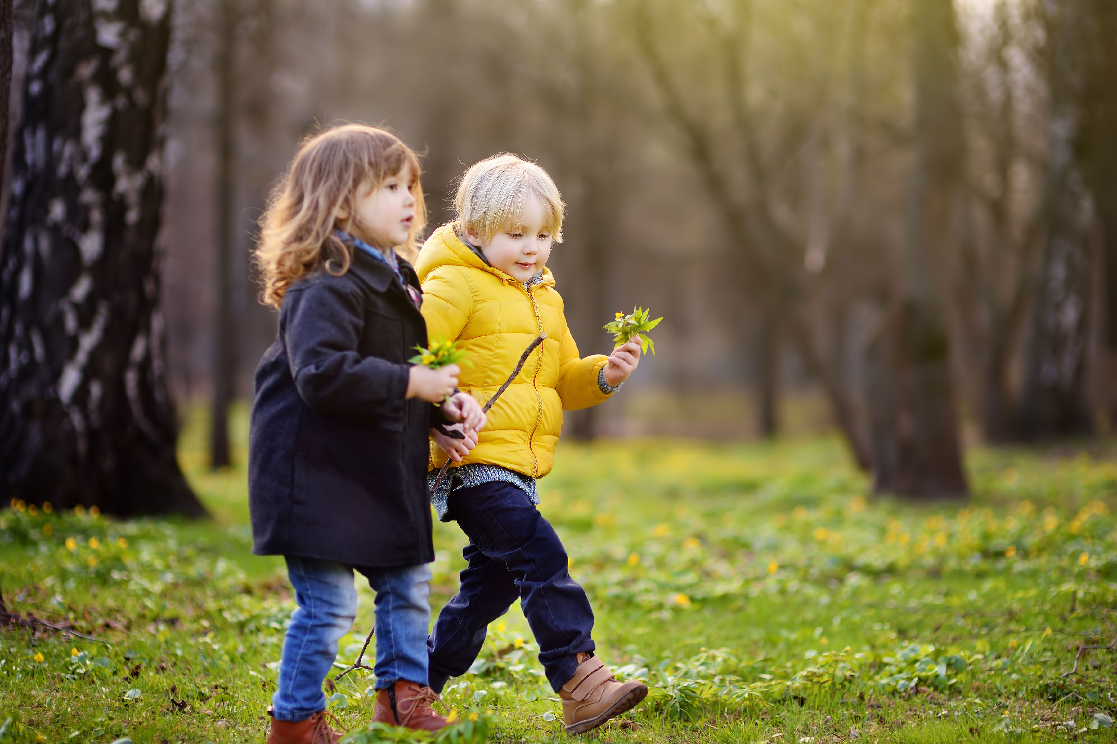 Zwei Kinder laufen mit Frühlingsblumen in der Hand durch einen Park