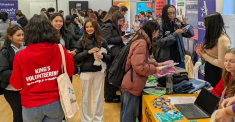 Loads of students are in a busy hall speaking to each other .