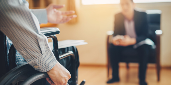 Mensch in Hemd sitzt im Rollstuhl einer Person gegenüber