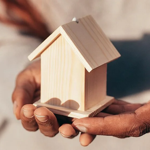 Hand, die ein kleines Holzhaus hält