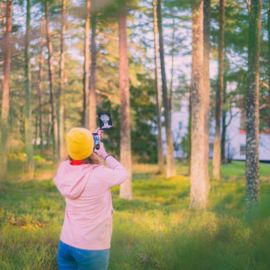 Henkilö metsässä ottamassa kuvaa puhelimella taidekortista.