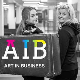 Kaksi naista ja matkalaukku, jossa lukee AIB Art in Business.