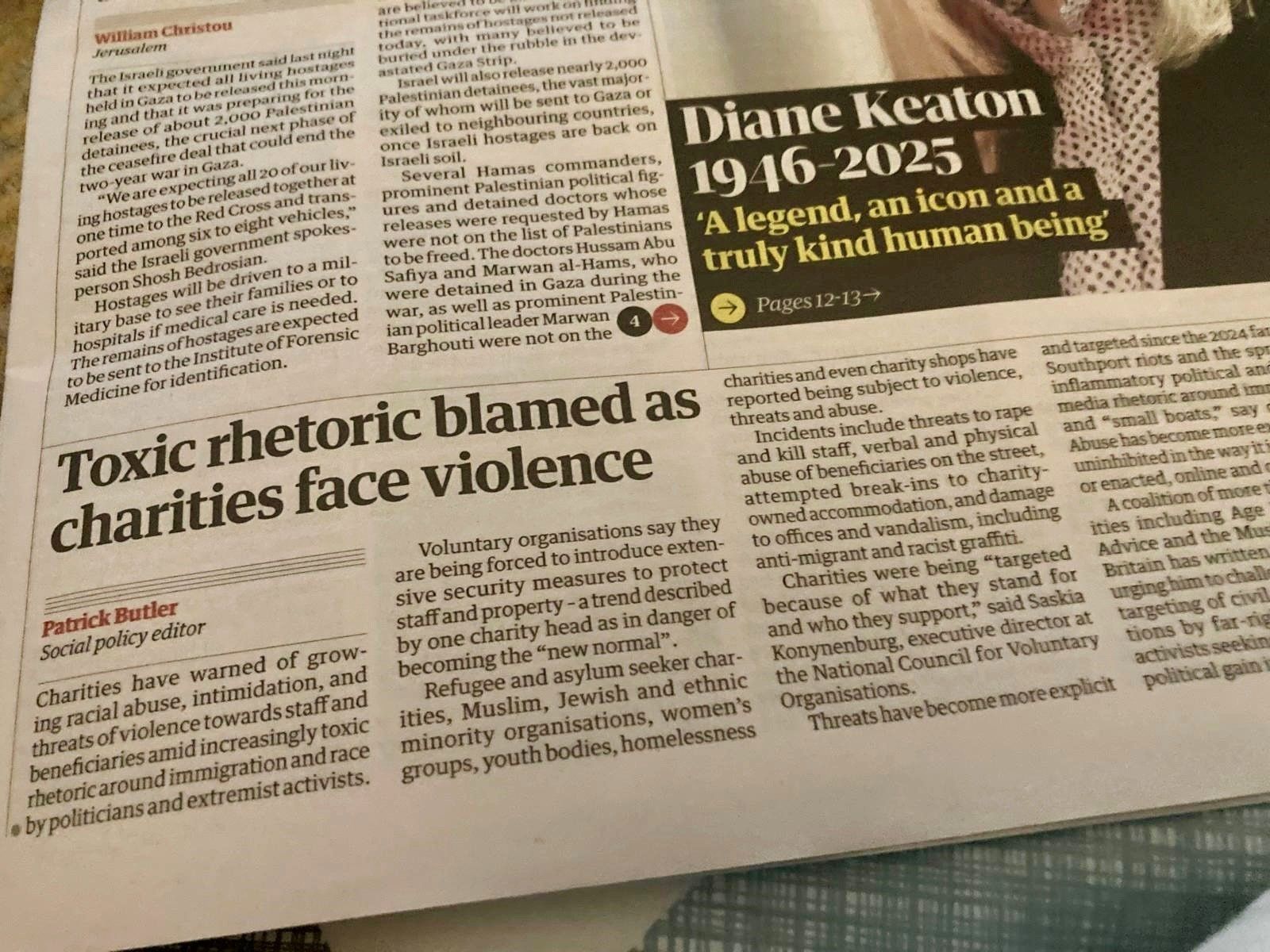 A newspaper page showing several articles. The main headline reads “Toxic rhetoric blamed as charities face violence,” written by Patrick Butler, Social policy editor. The article discusses threats and abuse against charities amid growing toxic rhetoric about immigration and race. Above it, there is a story headline reading “Diane Keaton 1946–2025: ‘A legend, an icon and a truly kind human being,’” suggesting an obituary piece. Another smaller article on the left mentions the Israeli government and hostage releases in Gaza. The newspaper appears to be The Guardian.