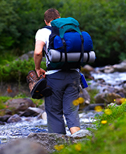 Mies reppureissaamassa luonnossa, kävelee puron yli,