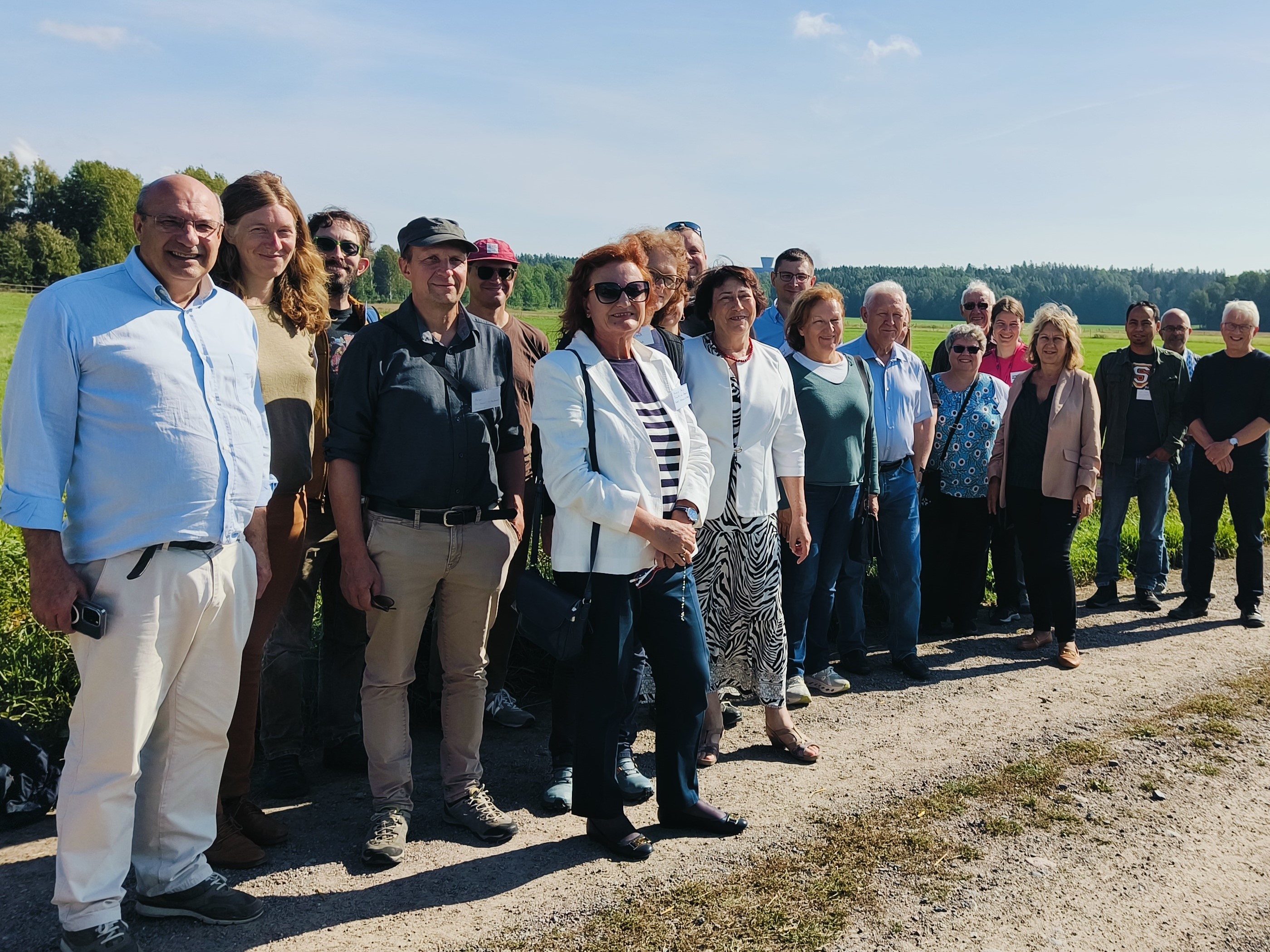 a group of people standing on a gravel road on front of a field and looking at the camera