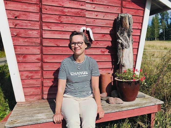 A woman sitting outside in the sunshine on front of a red hut