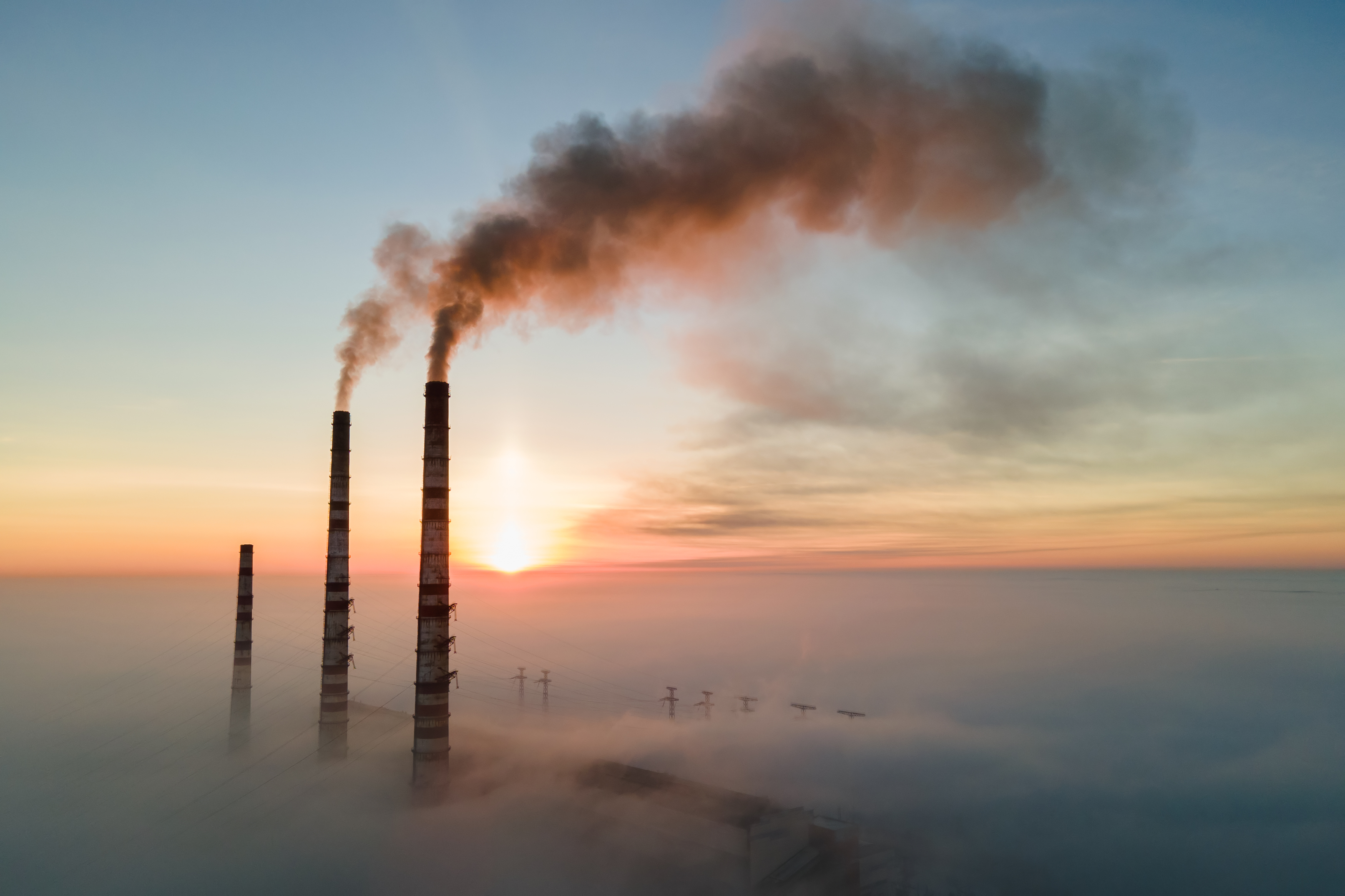 Voimalaitoksen piiput pilvien yllä auringon noustessa taustalla