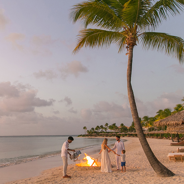 Family of four on Jumby Bay Beach around a bonfire