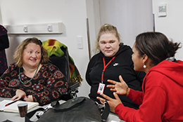 Kolme henkilöä istumassa pöydän ääressä ja keskustelemassa. Pöydällä reppu ja muistiinpanovälineet.