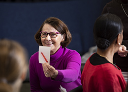 Henkilö istuu pitäen kädessään paperia, jossa on kynän kuva. 