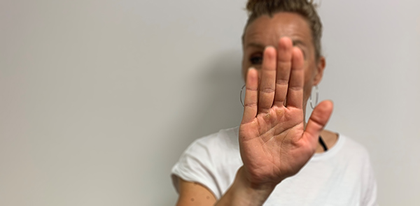 Henkiö seisoo ja pitää kättään kasvojensa edessä kämmenen sisäpuoli kameraa kohden. 