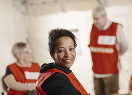 Kolme Punaisen Ristin vapaaehtoista, joista yksi istuu edessä kasvot kameraan päin ja kaksi on taustalla.