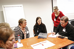 Kolme henkilöä istumassa pöydän ääressä ja keskustelemassa. Pöydällä reppu ja muistiinpanovälineet.