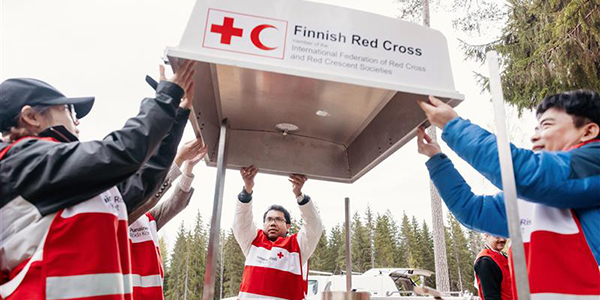Punaisen Ristin vapaaehtoisia nostamassa yhdessä katosta, jossa lukee Finnish Red Cross