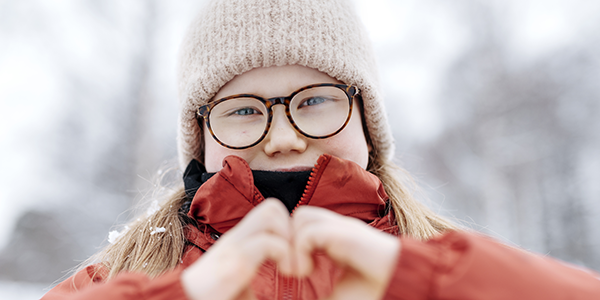 Hymyilevä lapsi talvisäässä kädet sydämenä edessä.