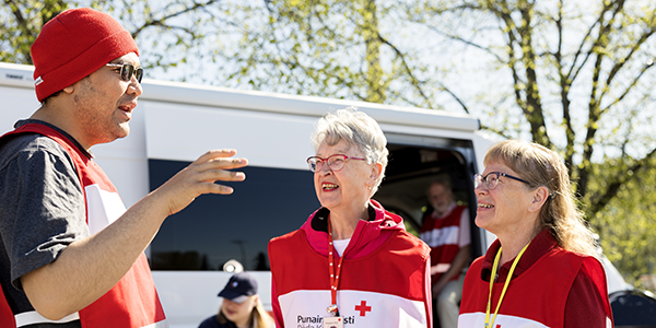 Kolme hymyilevää Punaisen Ristin vapaaehtoista ulkona juttelemassa.