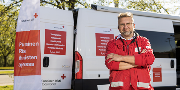 Henkilö seisomassa ulkona. Taustalla valkoinen retkeilyauto.