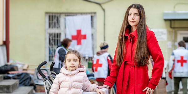 Aikuinen ja lapsi ulkona. Taustalla punaisia ristejä.