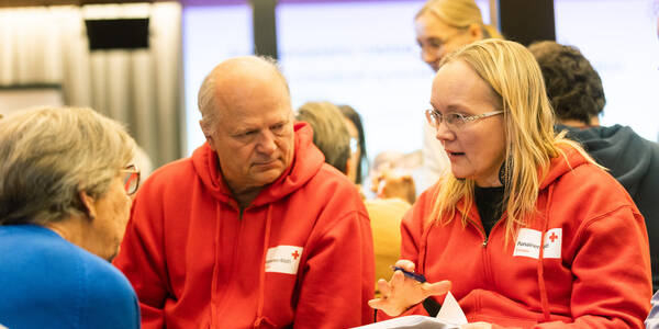 Kaksi Punaisen Ristin vapaaehtoista, mies ja nainen keskustelevat. Heillä on Punaisen Ristin hupparit päällä.