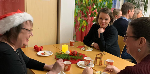 Kolme henkilöä juttelemassa pöydän ääressä. Pöydällä joulukoristeita sekä kertakäyttöastioita. 