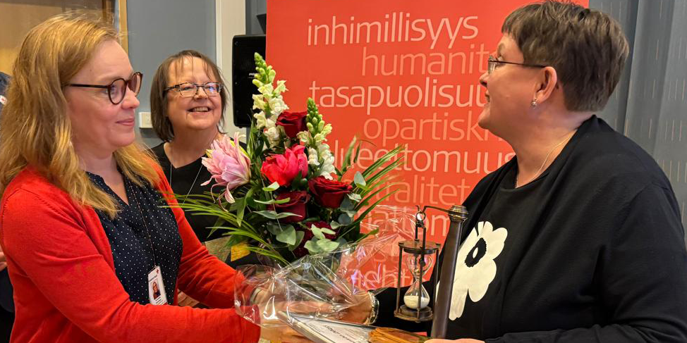 Henkilöitä ojentamassa kukkia kolmannelle henkilölle.