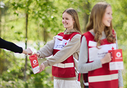 Kaksi hymyilevää henkilöä Punaisen Ristin liiveissä keräyslippaat käsissään.