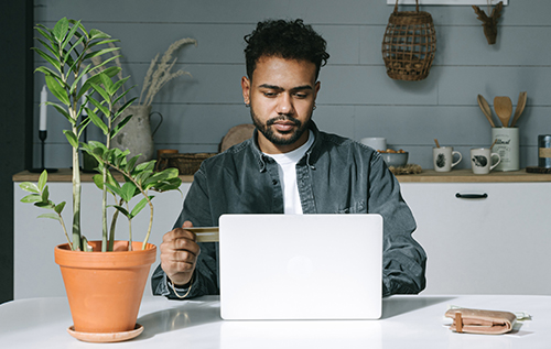 Man sitting behind a laptop with a credit card in his hand