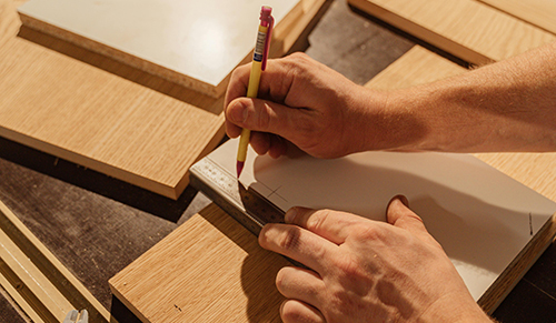 hands shown to draw a marking to a piece of plywood
